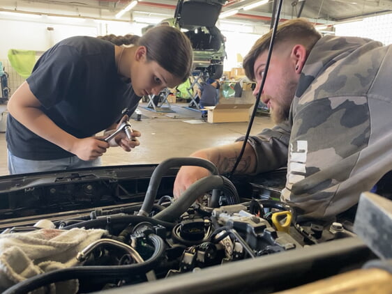 Bildunterschrift 2: Unter der Anleitung von Kfz-Mechatroniker Luca baut die Schülerin Carla den kaputten Motor eines Autos aus. (Foto: Handwerkskammer Region Stuttgart)