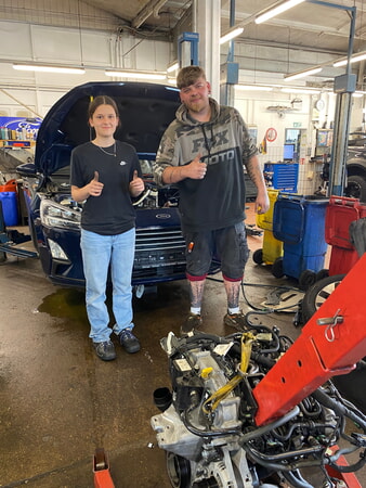 Bildunterschrift 4: Geschafft – nach mehreren Stunden Arbeit haben Carla und Kfz-Mechatroniker Luca den kaputten Motor ausgebaut. (Foto: Handwerkskammer Region Stuttgart)